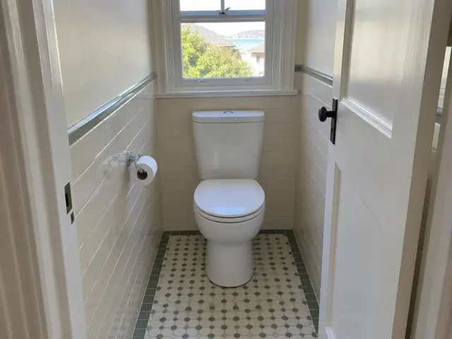 Clean white toilet in a small tiled bathroom with a window and patterned floor in Dover Heights