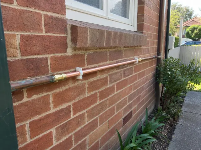Repaired copper water pipe on a brick exterior wall with garden path in Rose Bay